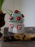 Ceramic house-shaped tea light holder with red flowers on a textured surface