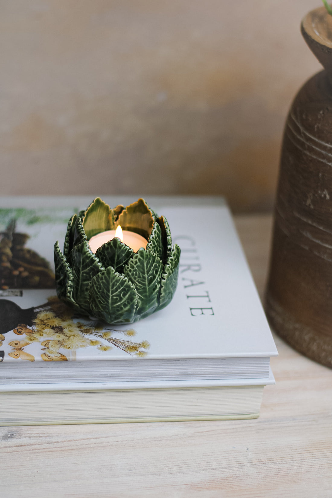 A green leaf-shaped tea light holder made of metal, placed on top of a book.