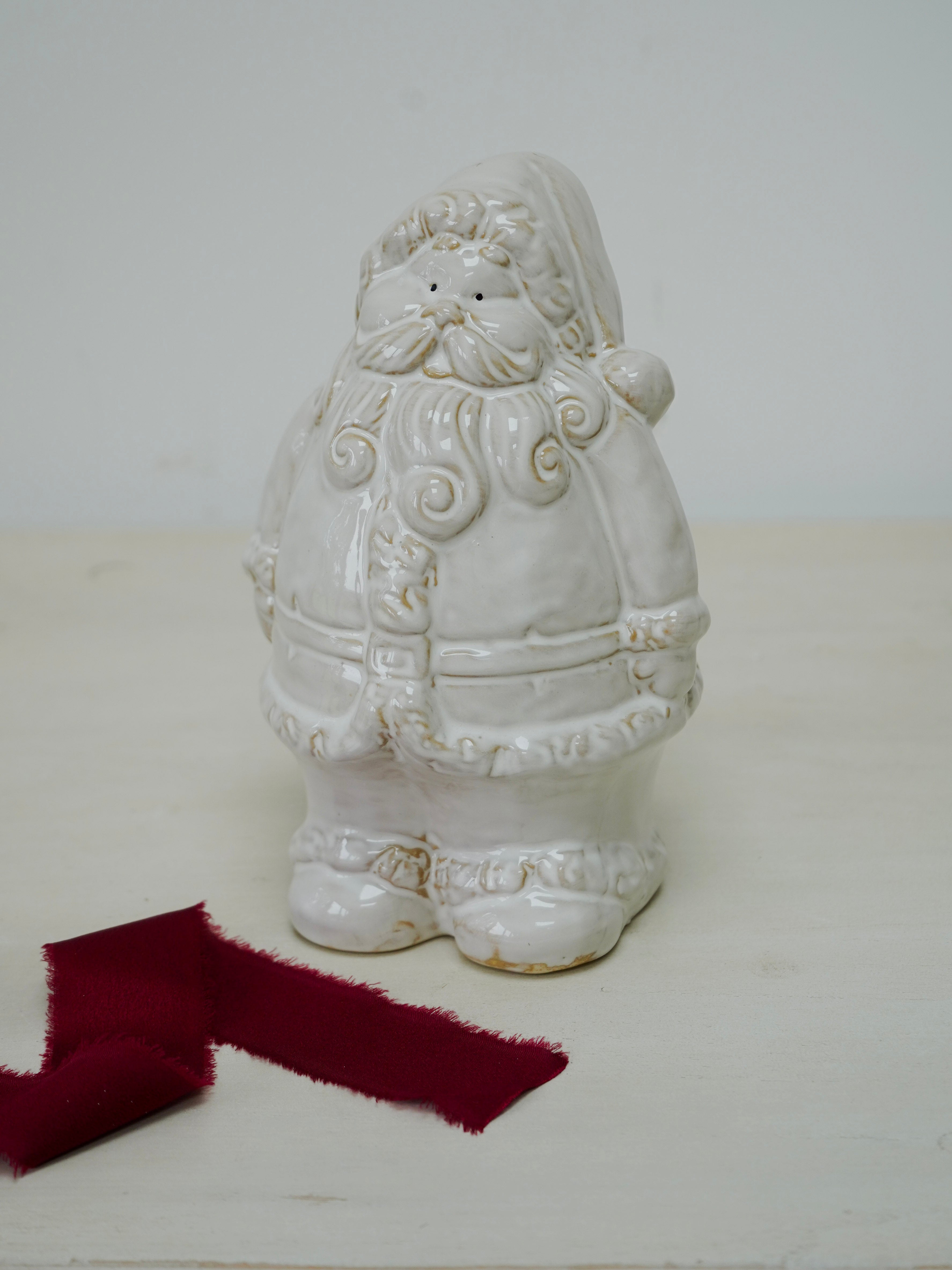 White ceramic Santa Claus figure on a white surface with a red ribbon.