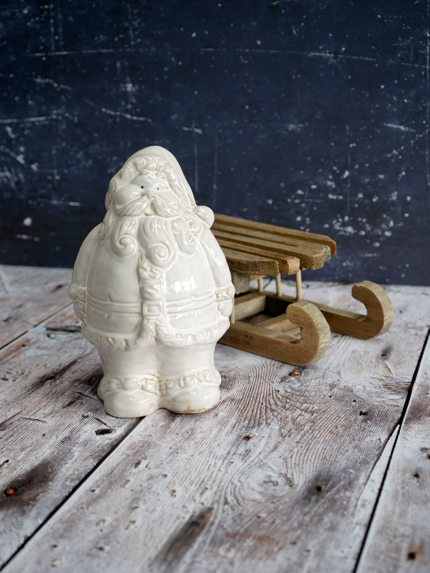 White ceramic Santa Claus figure with a wooden sleigh on a rustic wooden surface.
