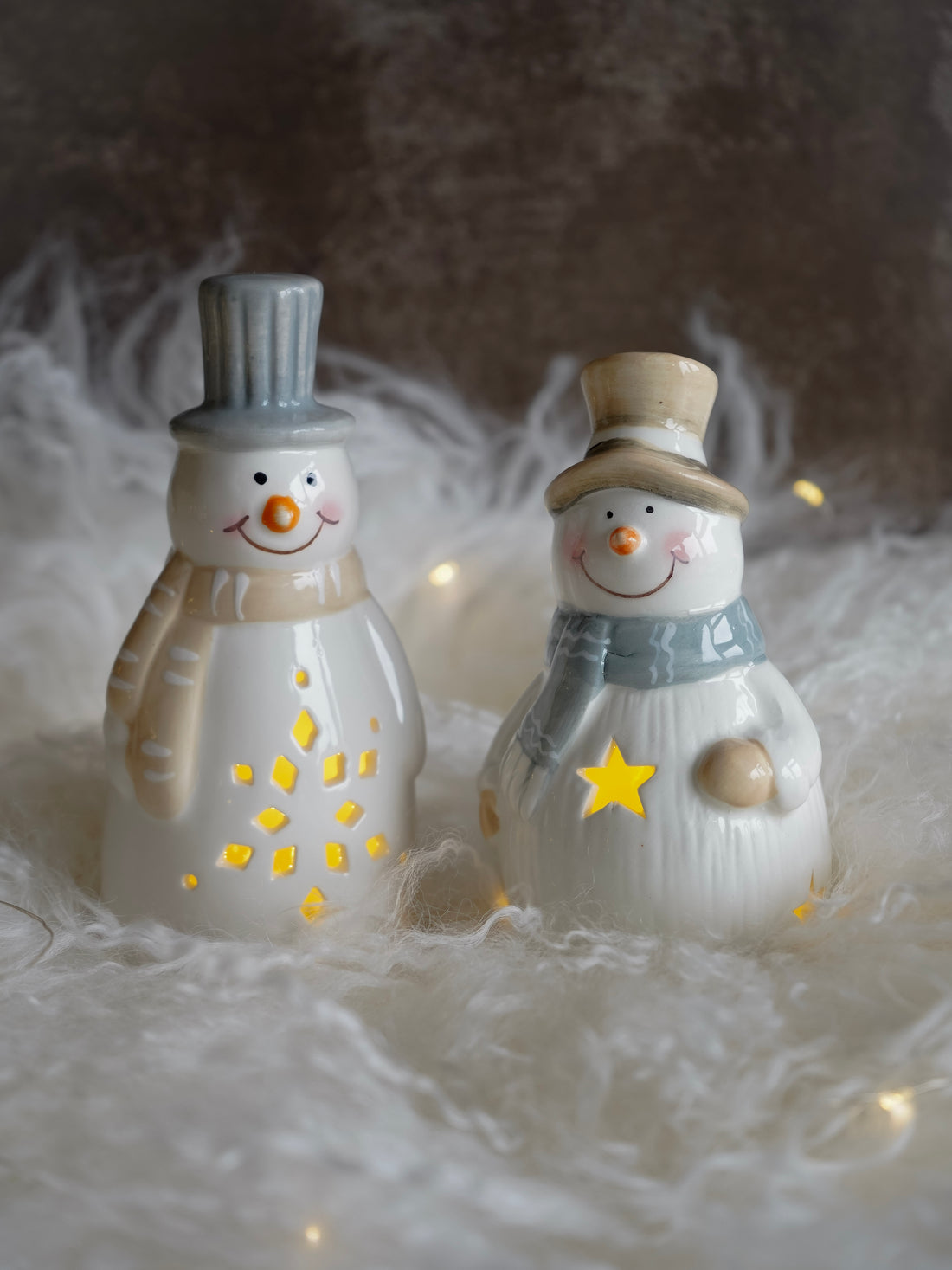 Two decorative snowmen with top hats and scarves on a soft, textured surface.