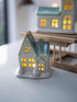 Ceramic house-shaped lantern with glowing interior on a white surface.