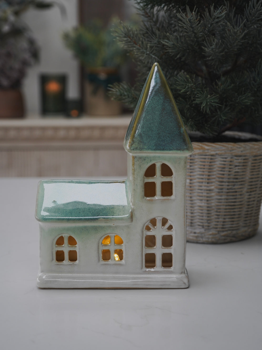Ceramic chapel shaped lantern with a green roof on a white surface.