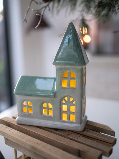 Ceramic chapel-shaped lantern with glowing interior on a wooden surface