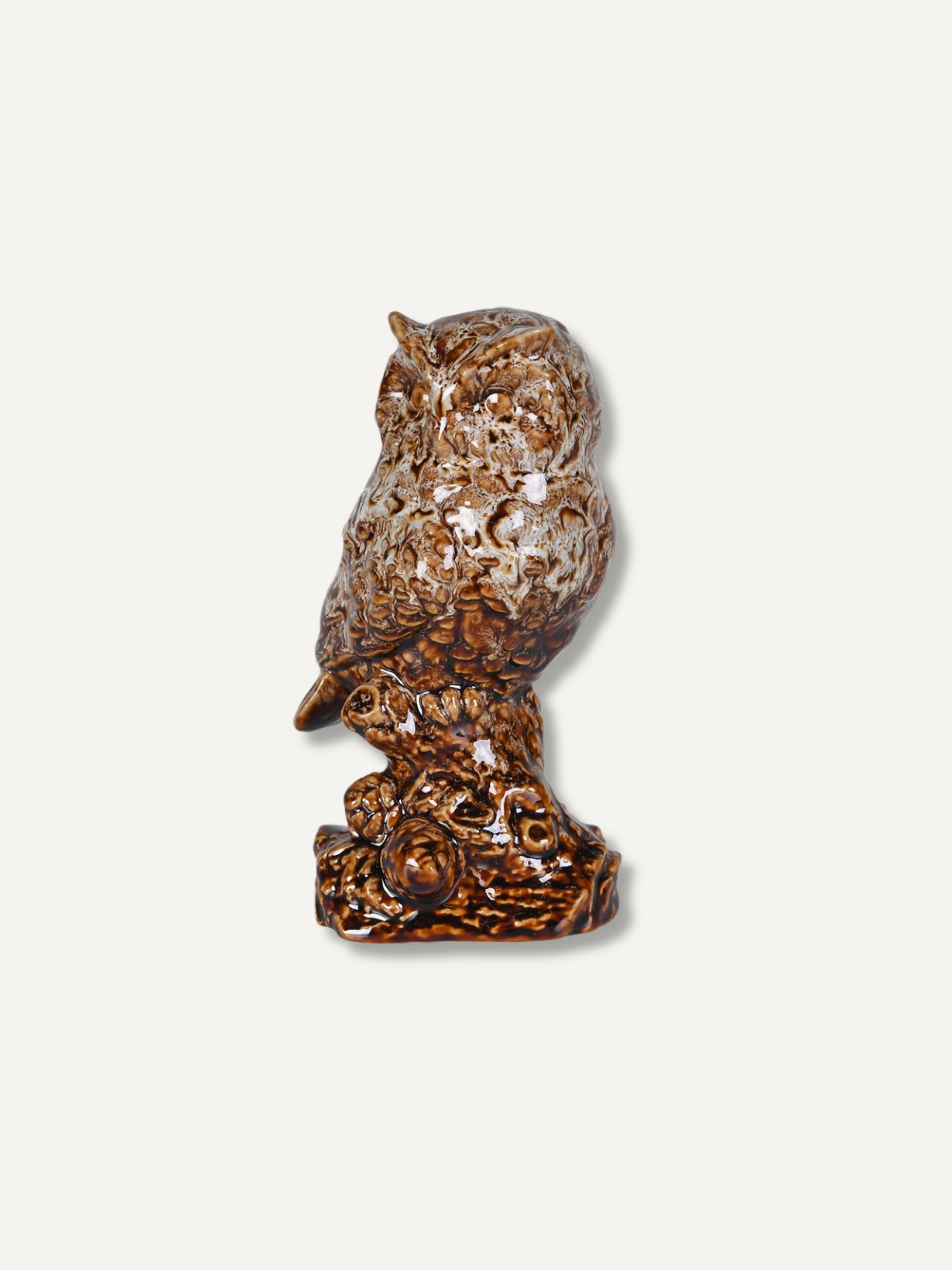 A small owl figurine with a textured, carved appearance in brown and beige tones, perched on a decorative base against a plain light background.