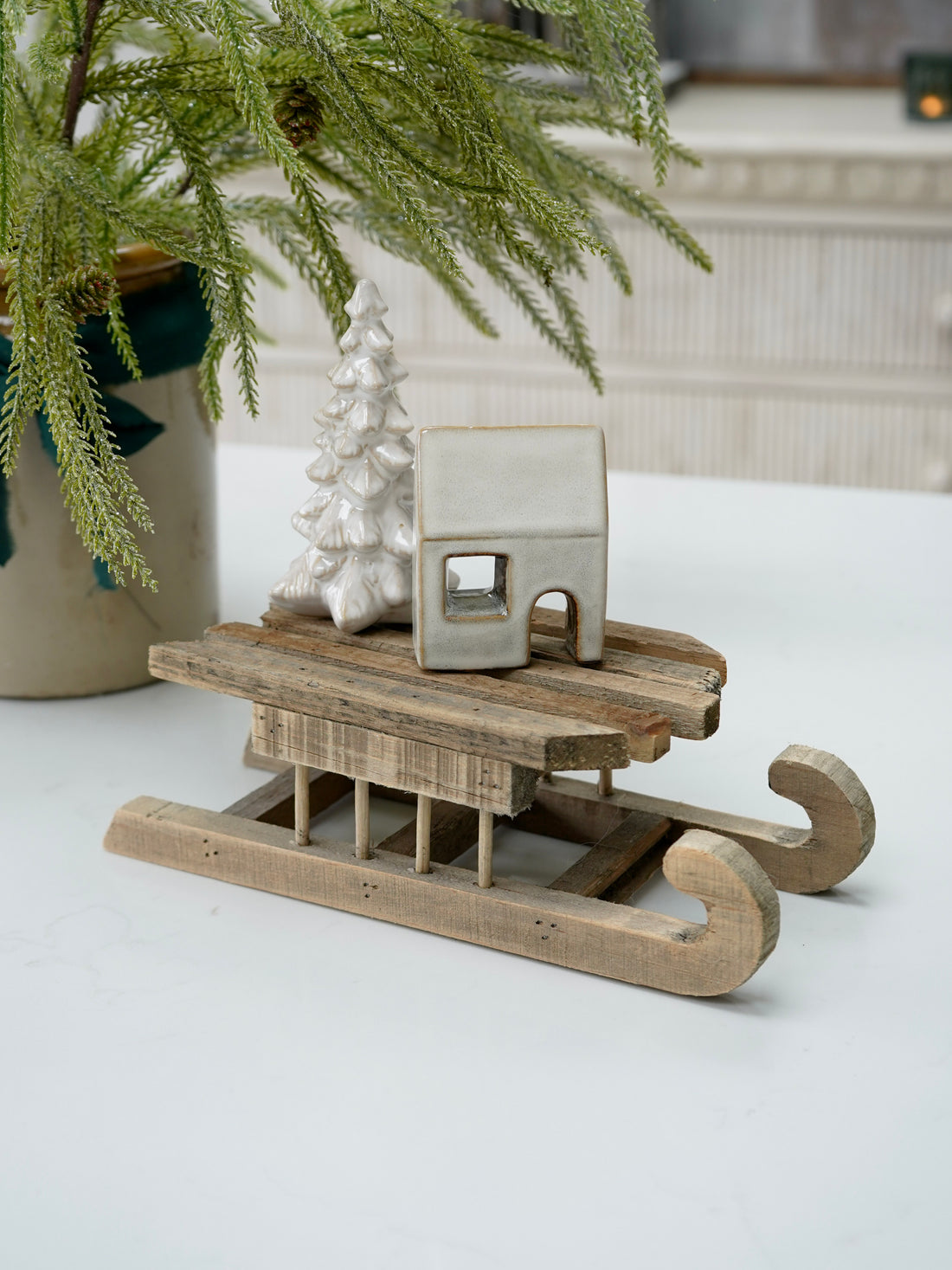 Wooden sled with a small house model and decorative tree on a white surface.