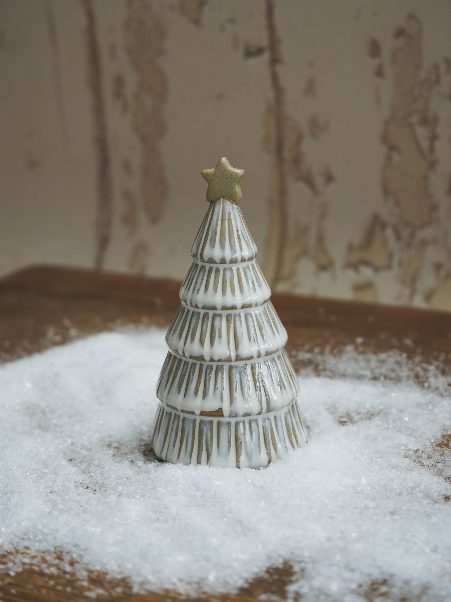 Decorative Christmas tree figurine with a star on top, placed on a snowy surface.