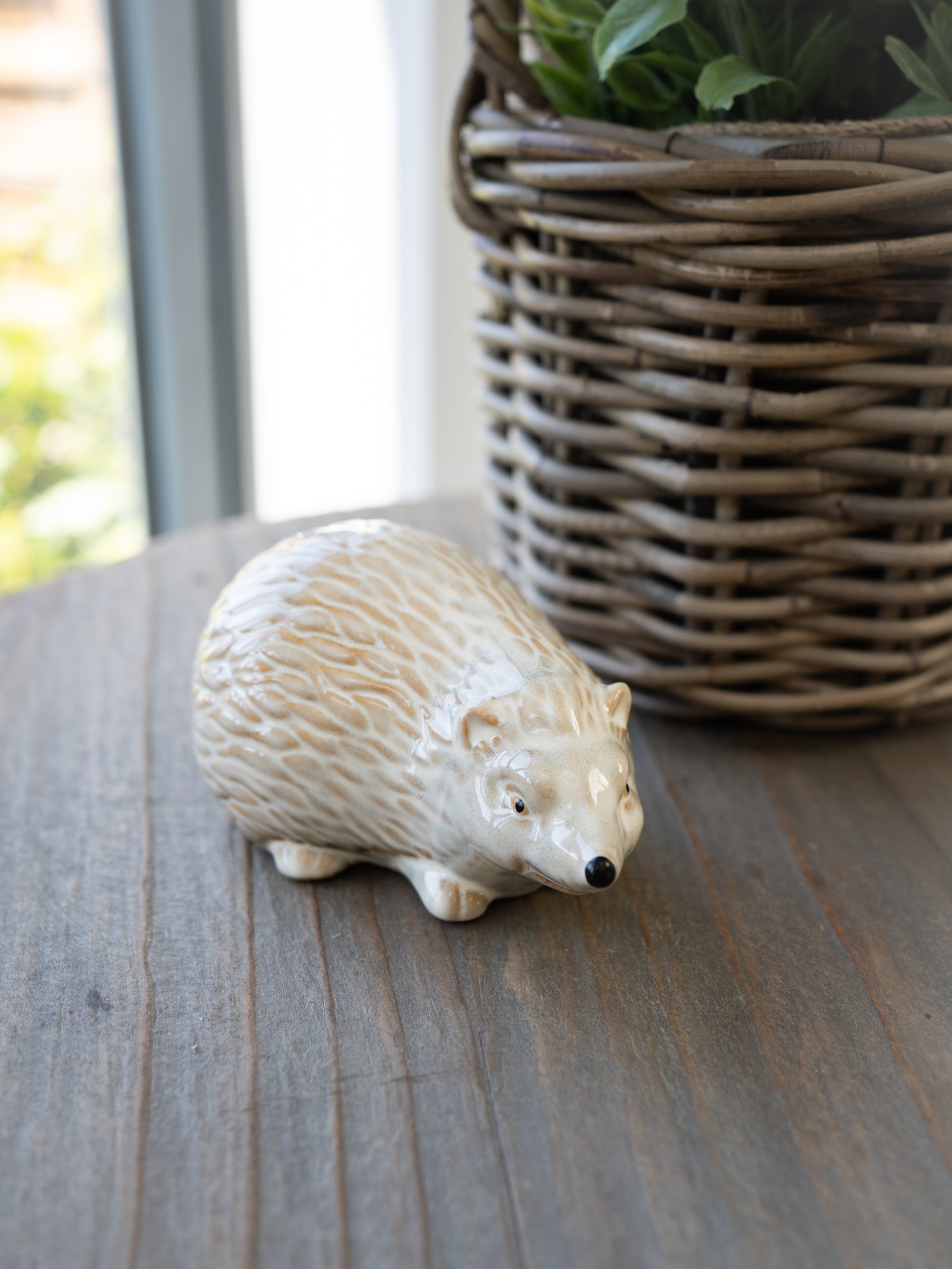 Ceramic hedgehog figurine on a wooden surface with a wicker basket in the background.