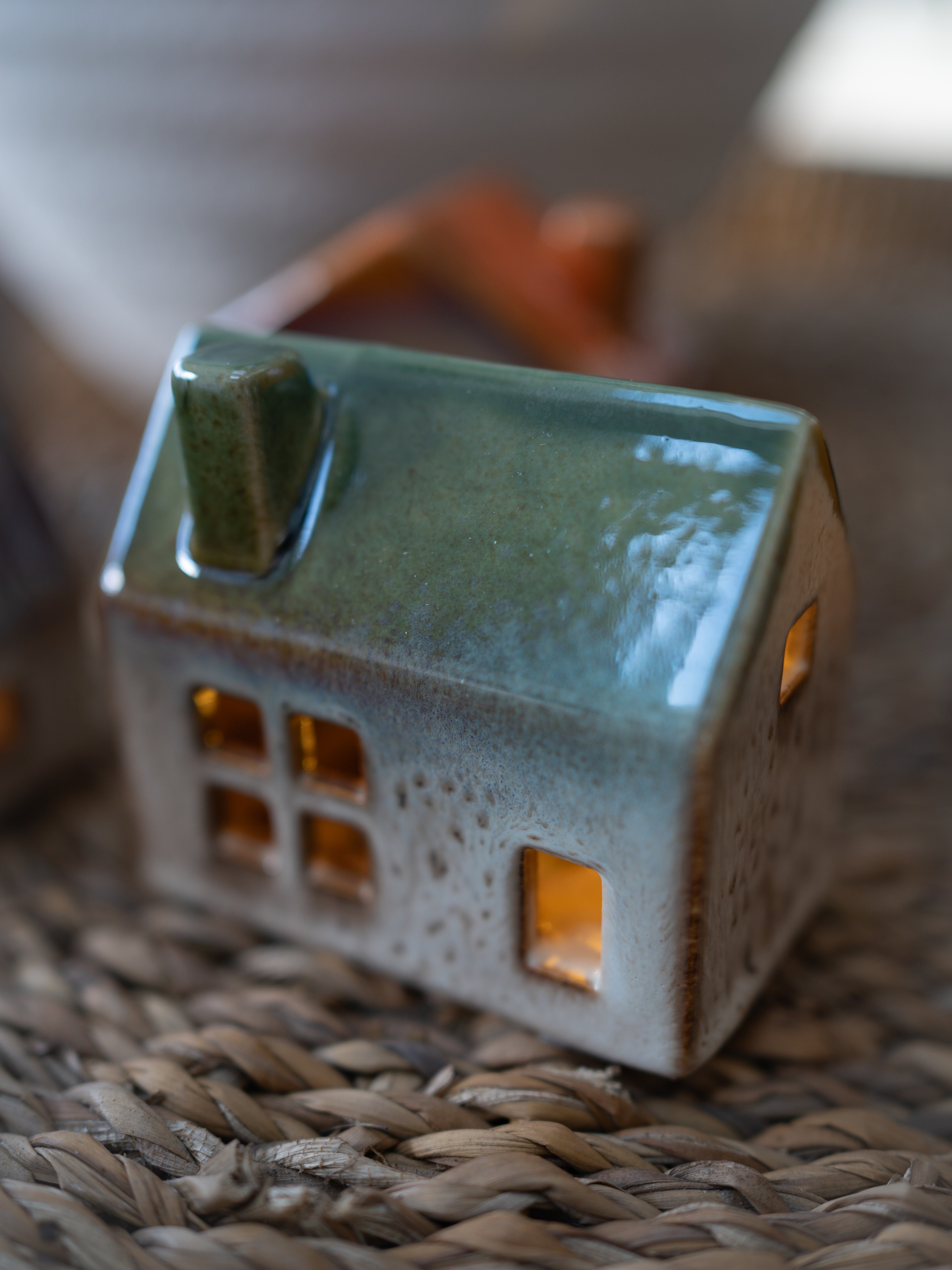 Ceramic house-shaped lantern with a green roof on a woven surface