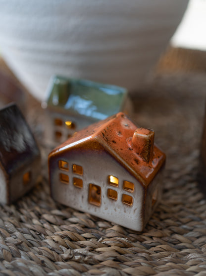 Small ceramic house with a brown roof on a woven surface