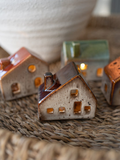 Small ceramic house-shaped candles on a woven surface with a blurred background