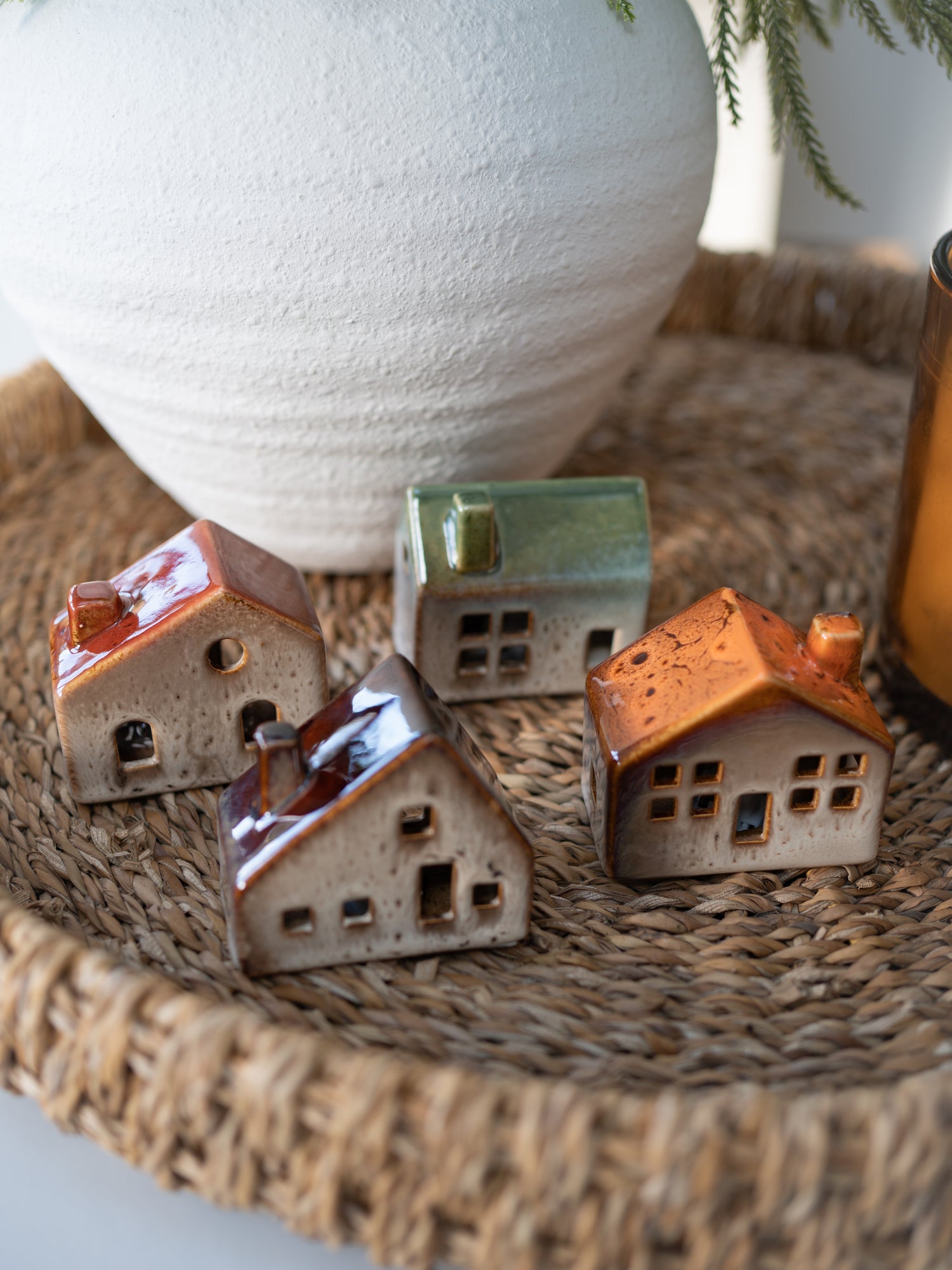 Small ceramic houses on a woven surface with a large white vase in the background