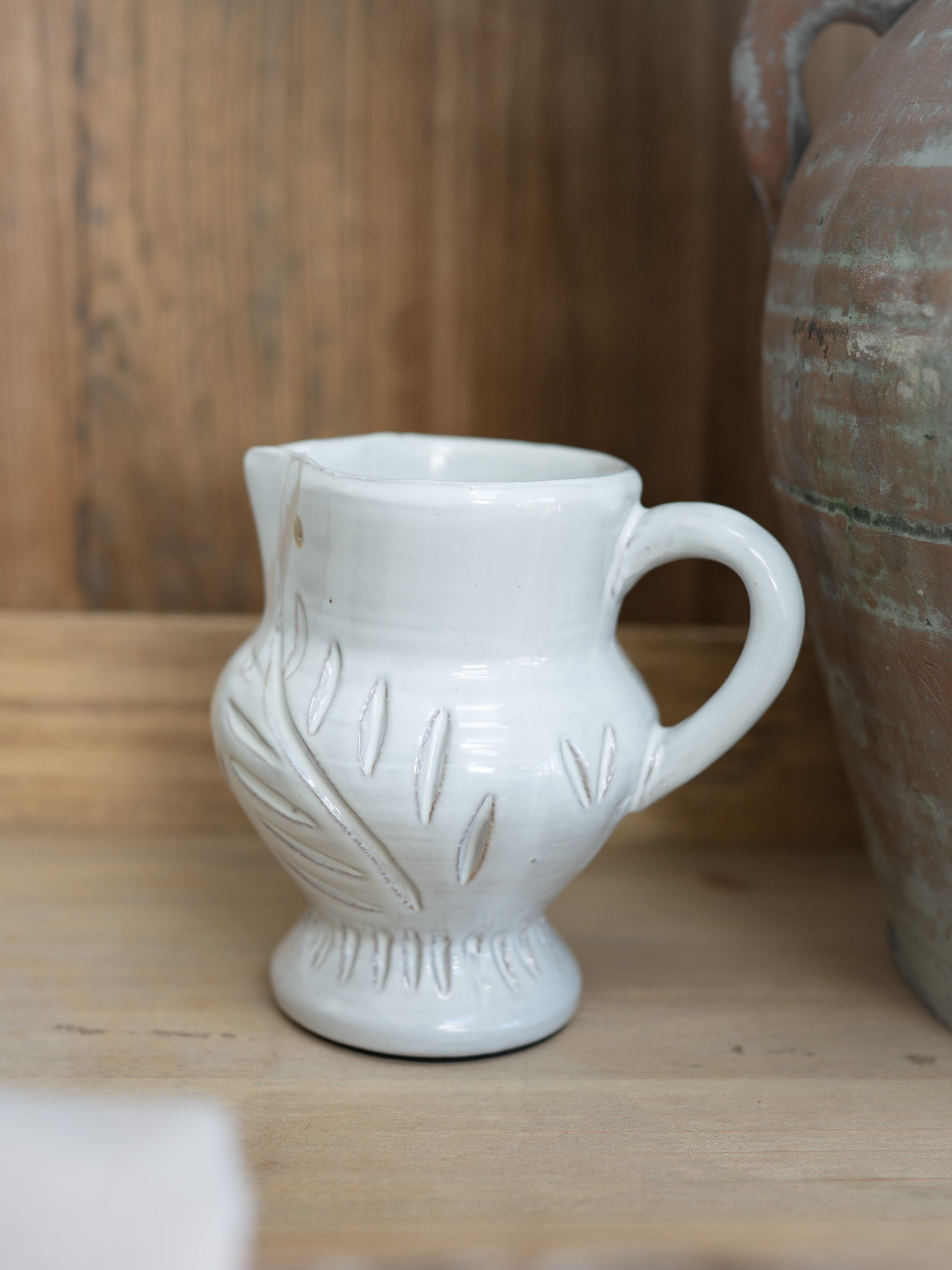 White ceramic pitcher with decorative patterns on a wooden surface
