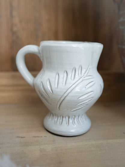 White ceramic pitcher with leaf patterns on a wooden surface