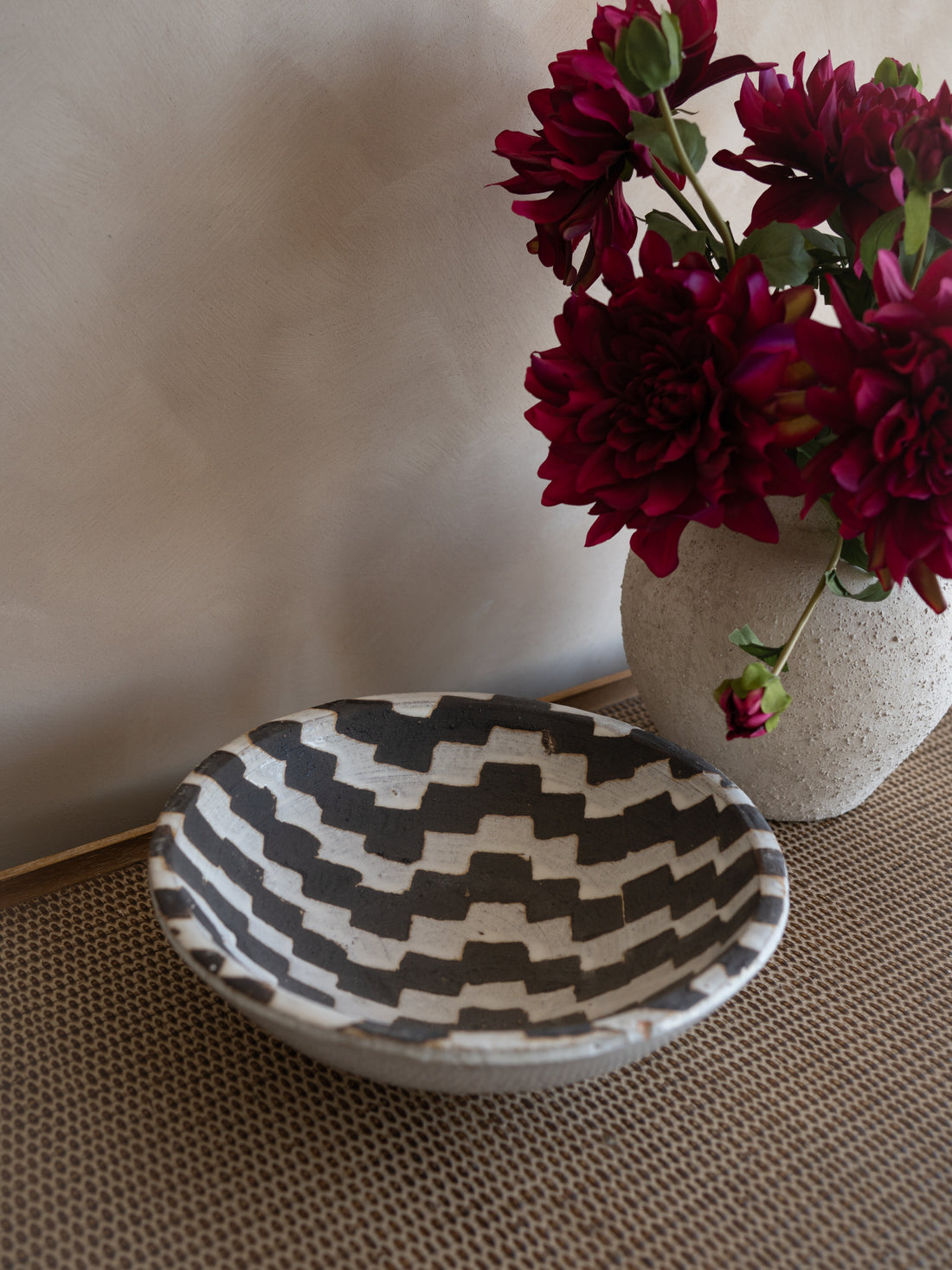 Decorative bowl with geometric pattern next to a vase of red flowers on a textured surface.