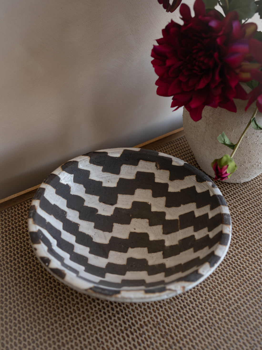 Black and white patterned bowl on a textured surface with a vase of red flowers in the background.