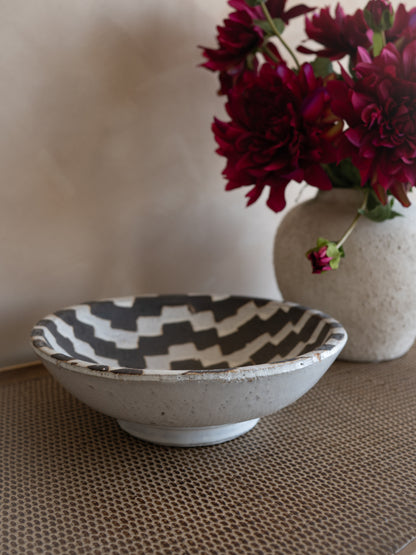 Ceramic bowl with a geometric pattern next to a vase with red flowers on a textured surface.