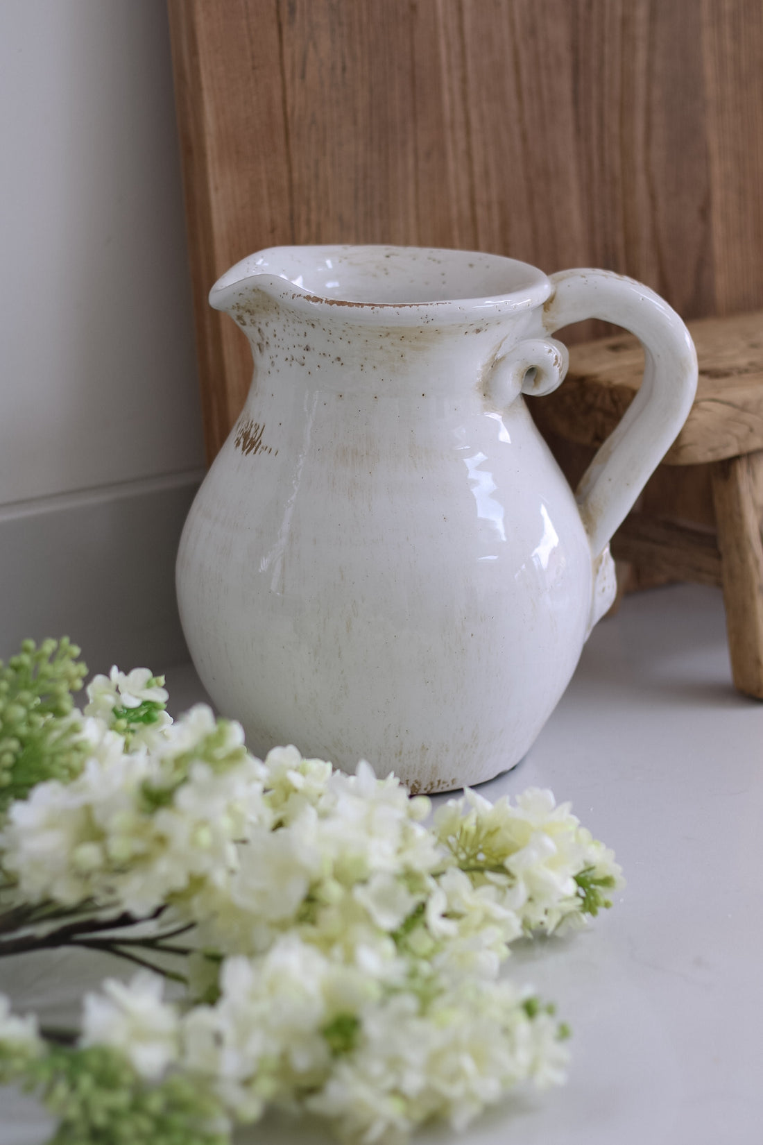 White ceramic pitcher on a surface with flowers in the foreground