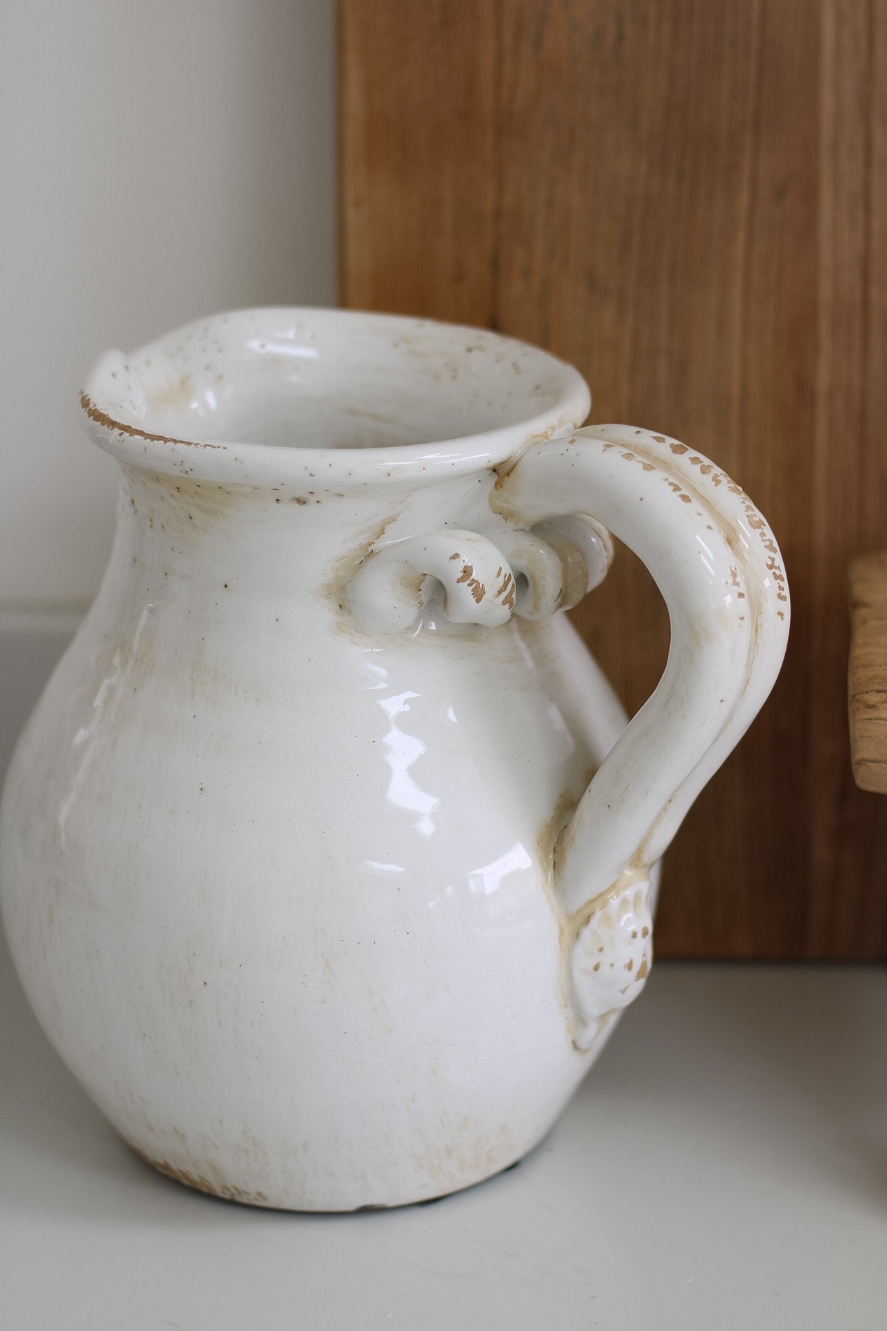 White ceramic pitcher with a handle on a wooden surface
