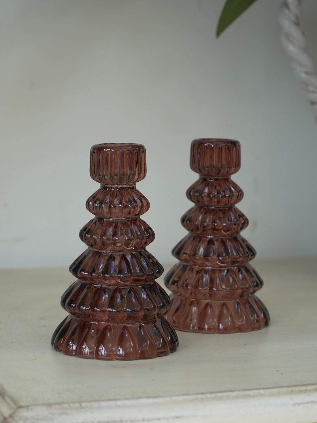 Two brown glass christmas tree candle holders on a white surface with a neutral background
