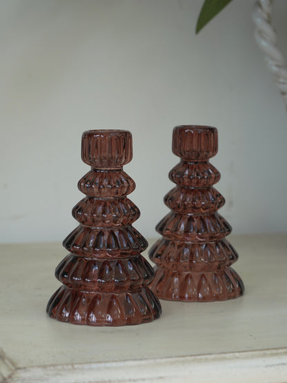Two brown glass christmas tree candle holders on a white surface with a neutral background