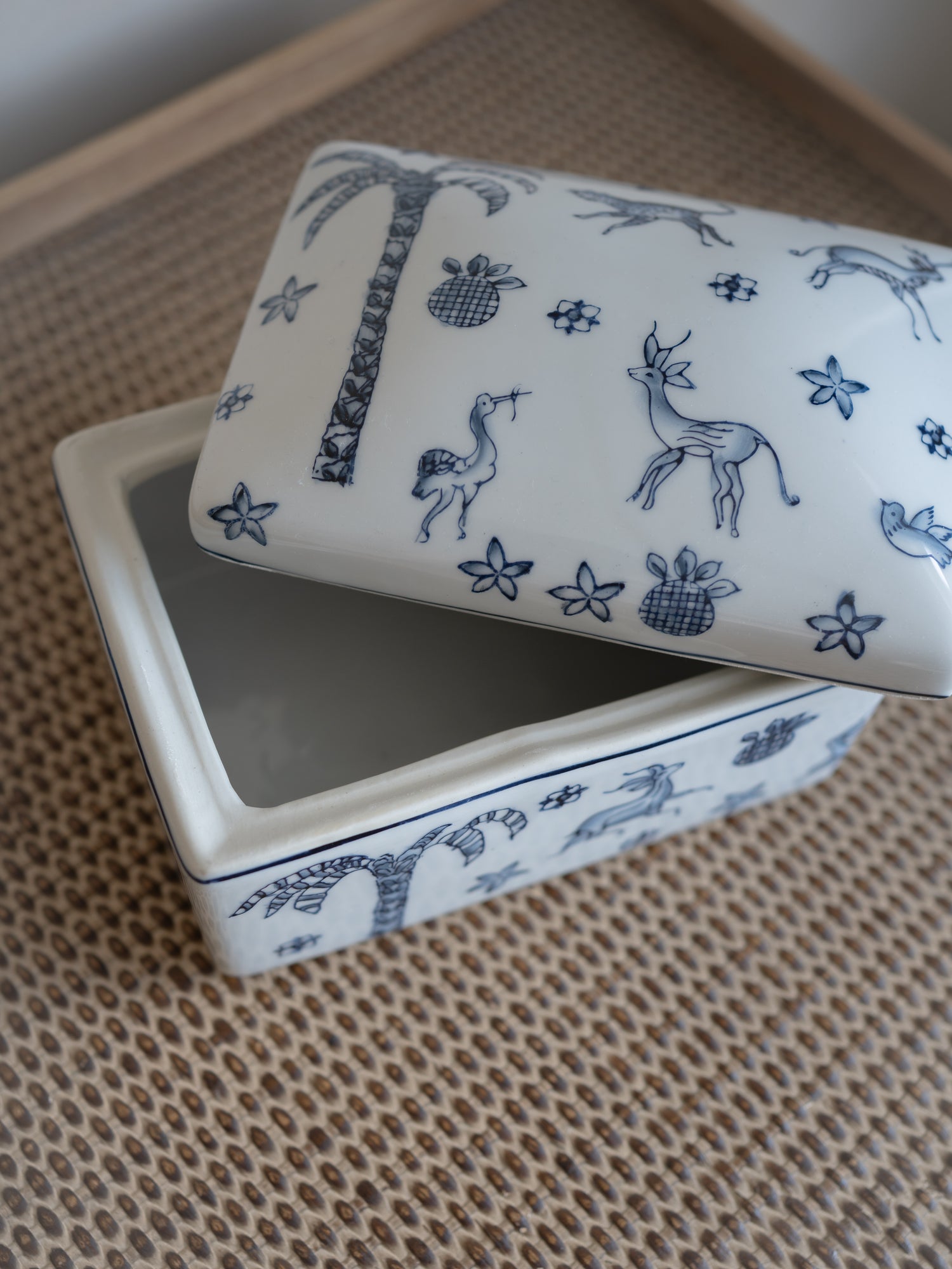 Decorative white ceramic  box with blue animal and plant patterns on a textured surface