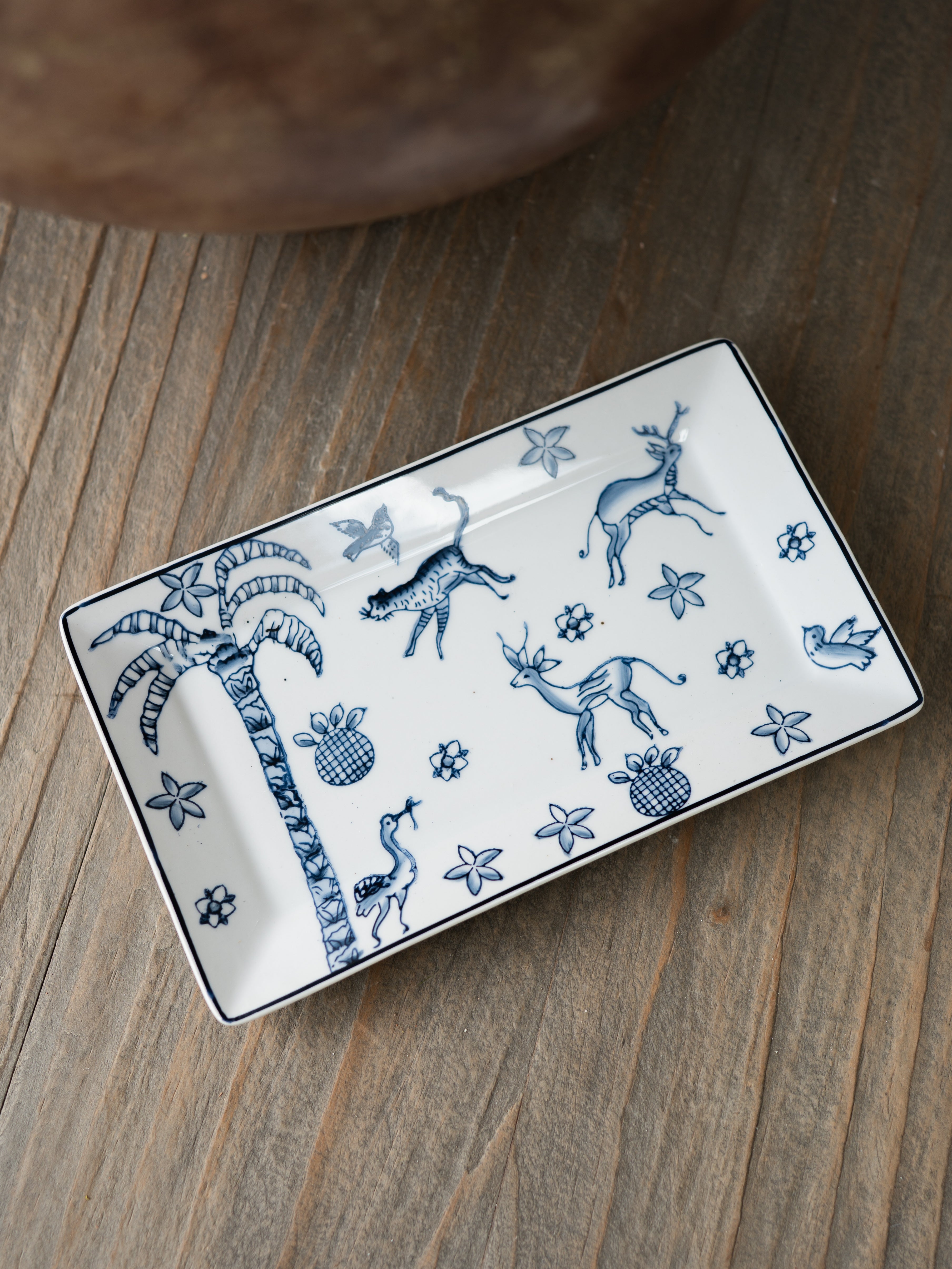 Rectangular ceramic trinket tray with blue animal and plant designs on a wooden surface