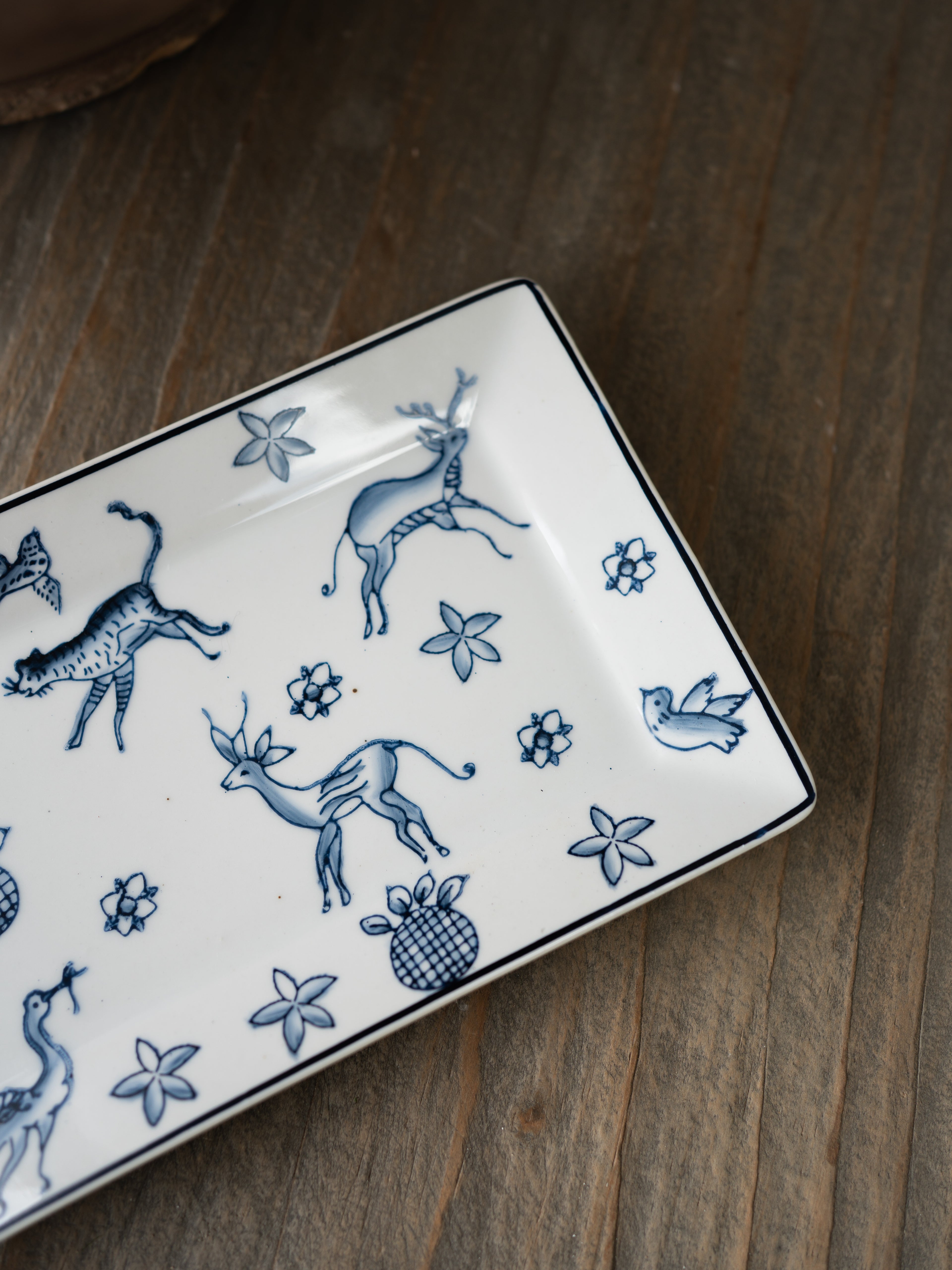 Rectangular ceramic trinket tray with blue animal and floral patterns on a wooden surface