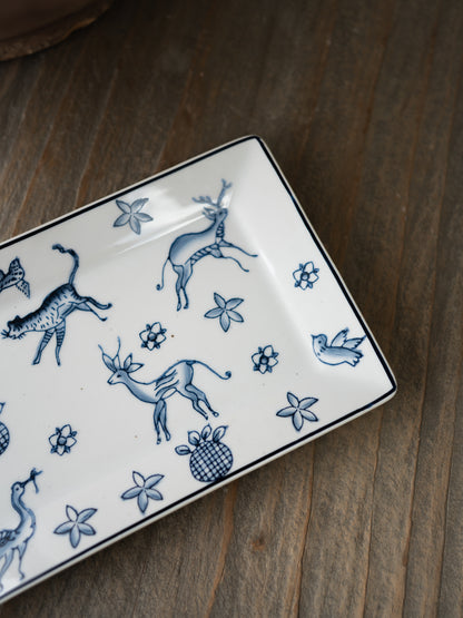 Rectangular ceramic trinket tray with blue animal and floral patterns on a wooden surface