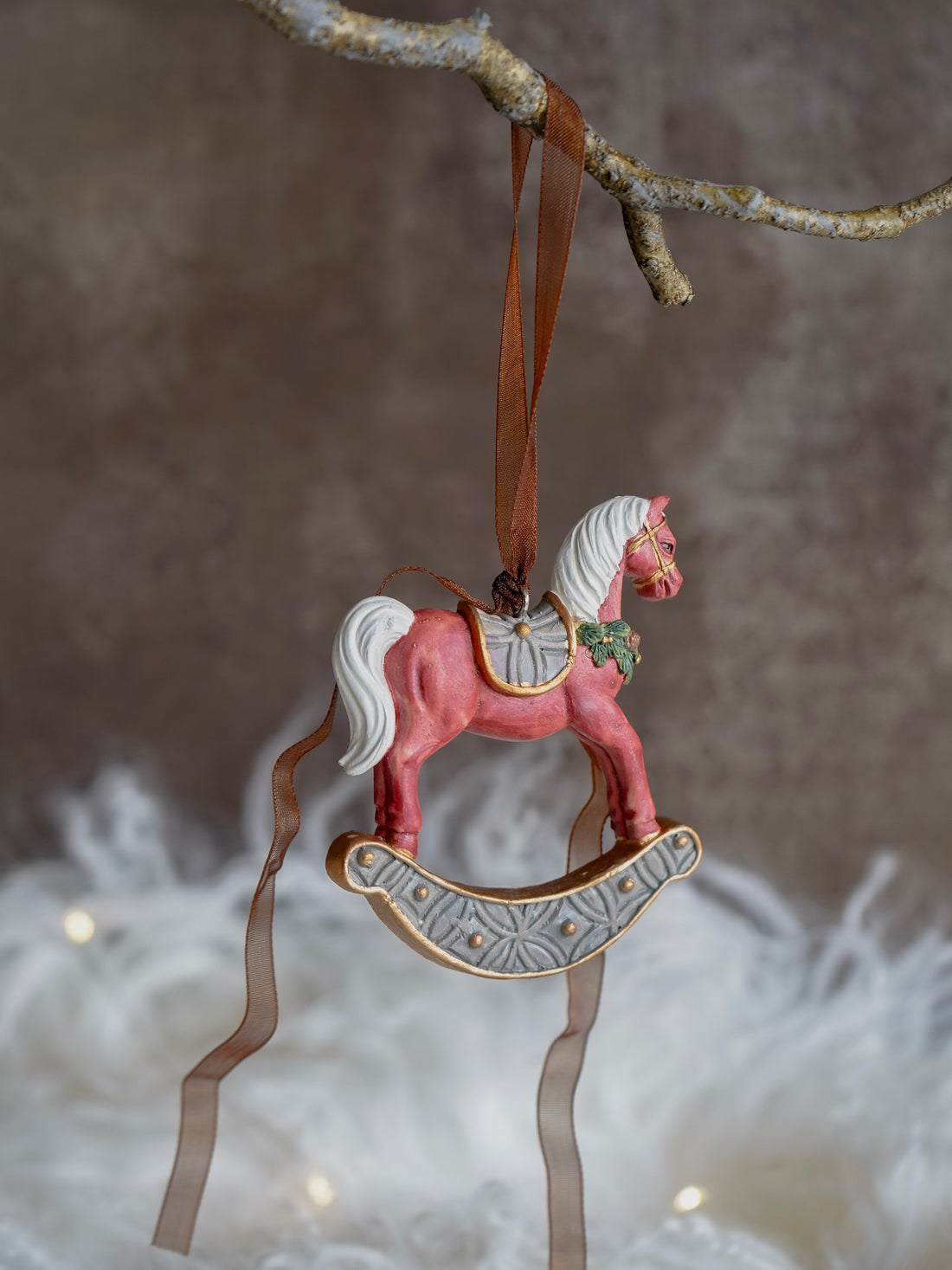 Decorative rocking horse ornament hanging from a branch with a soft blurred background