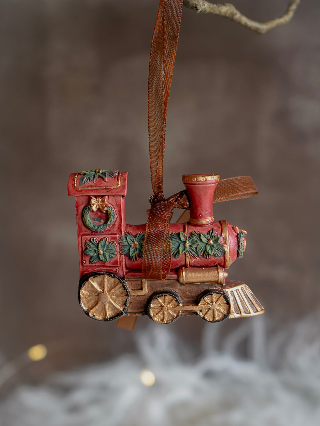 Decorative train ornament with a brown ribbon against a blurred background