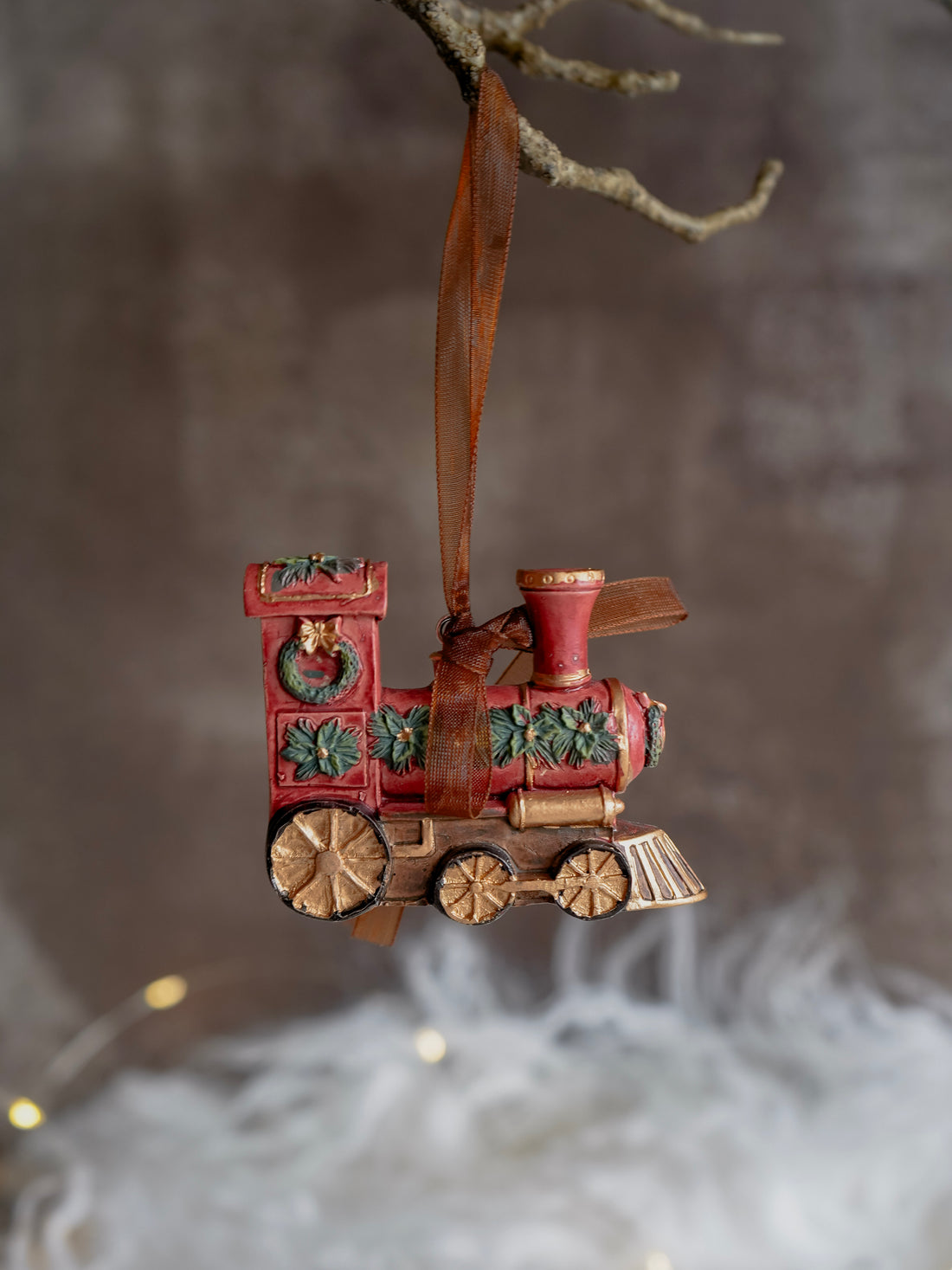 Decorative train ornament hanging from a branch with a blurred background