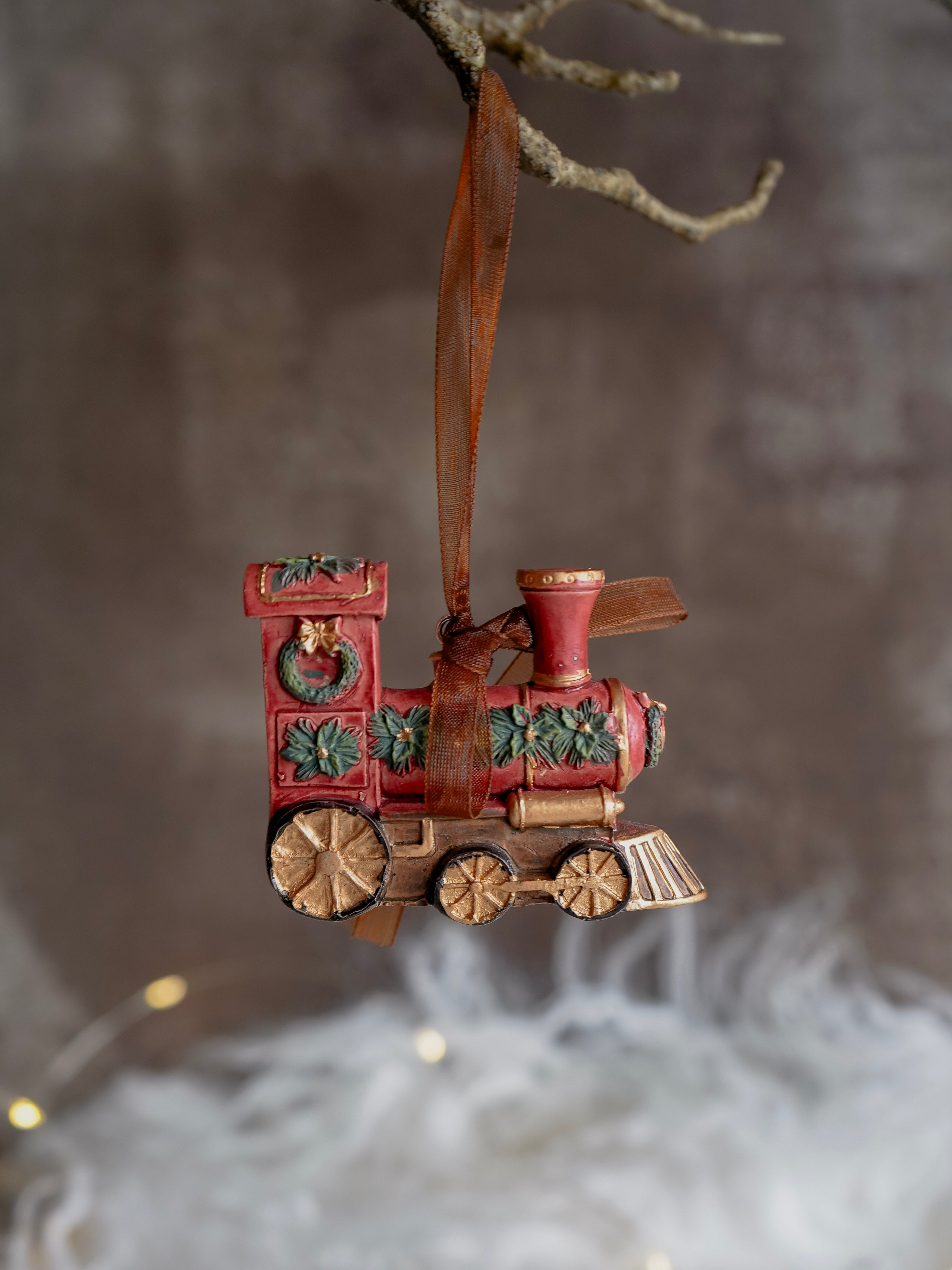 Decorative train ornament hanging from a branch with a blurred background