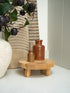Wooden stand with two small brown bottles on a light surface, with a neutral background.