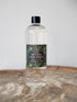 A clear bottle of Home Fragrance Citrus Verbena home fragrance diffuser refill oil with a black cap and a dark green botanical label, standing on a rustic wood slice against a light gray background.