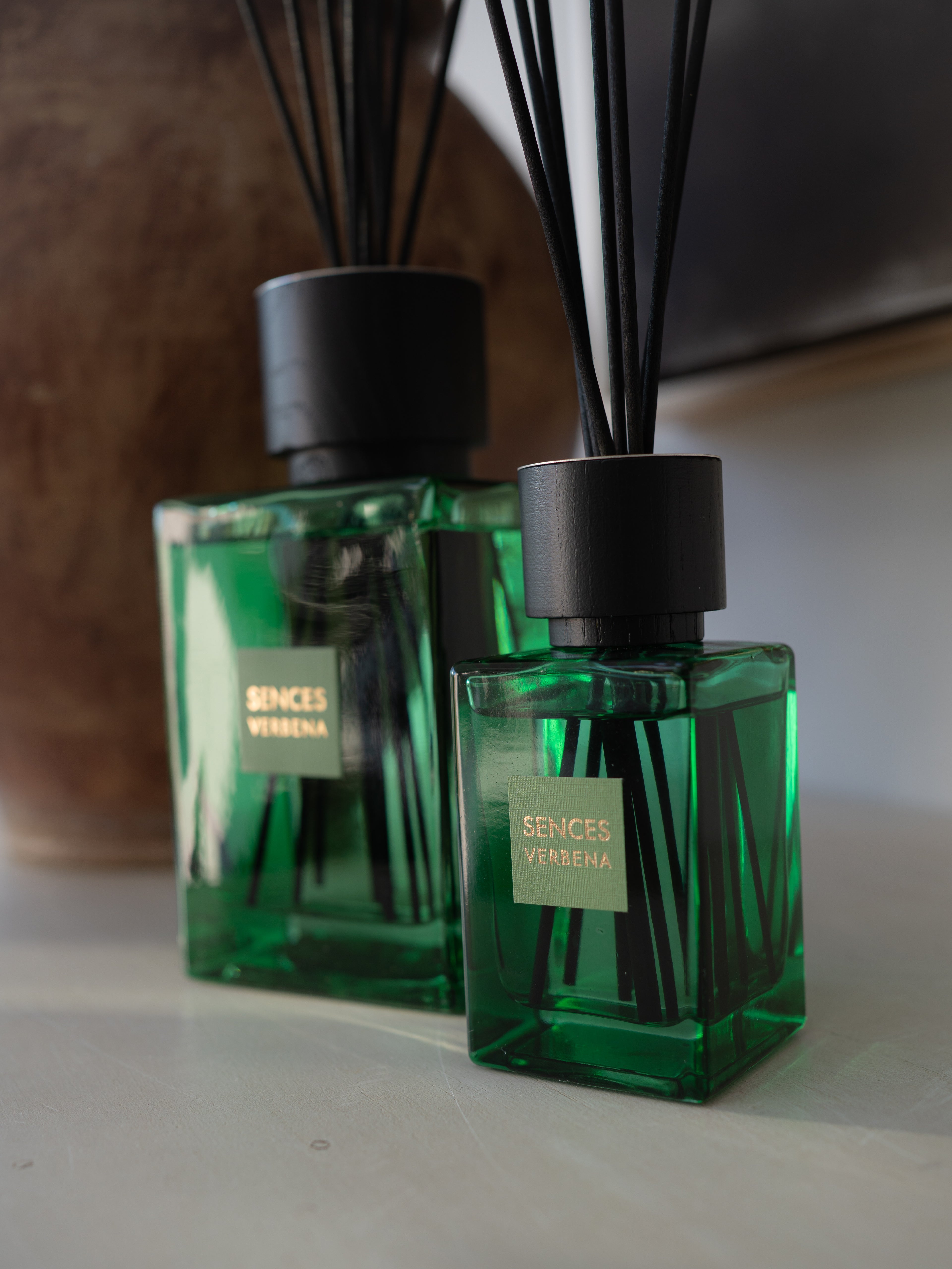Two green glass reed diffusers with black caps and reeds, labeled &