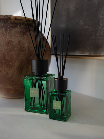 Two green glass reed diffusers with black caps and black reeds, labeled &