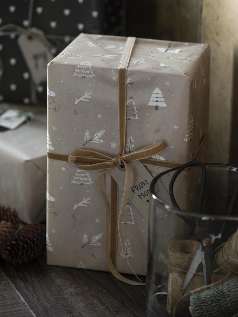 Gift wrapped in patterned paper with a bow, surrounded by festive decor.