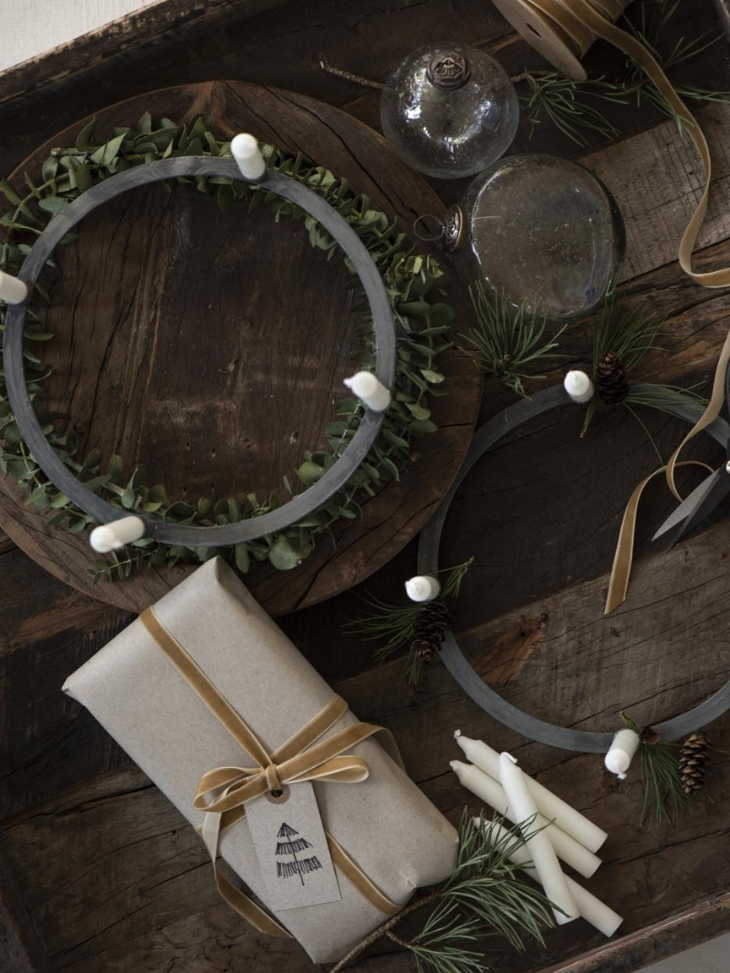 Decorative wreaths, candles, and a wrapped gift on a wooden surface with a rustic theme.