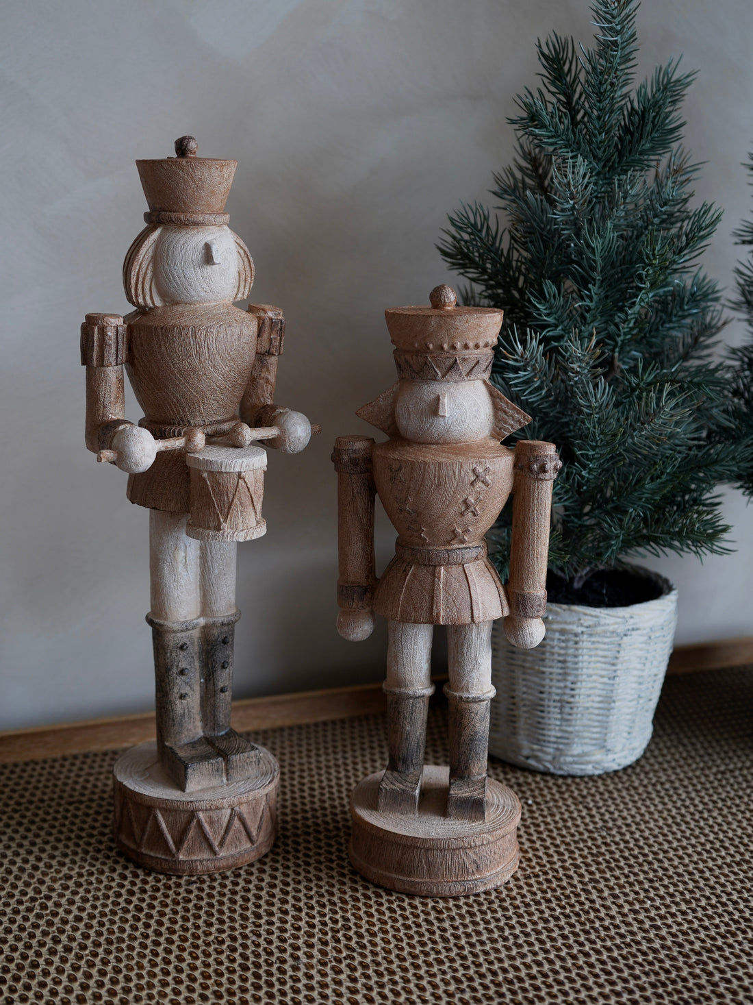 Two wooden nutcrackers on a textured surface with a plant in the background.