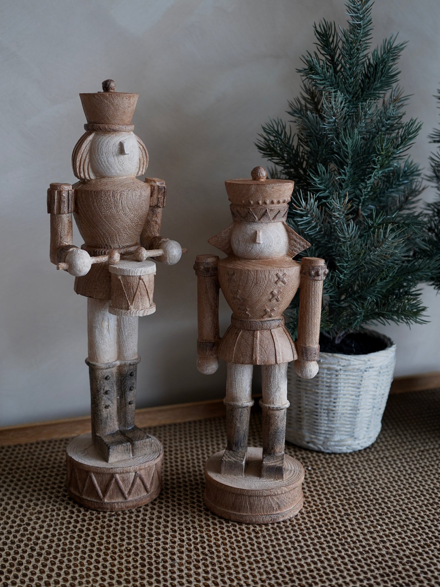 Two wooden nutcrackers on a textured surface with a plant in the background.