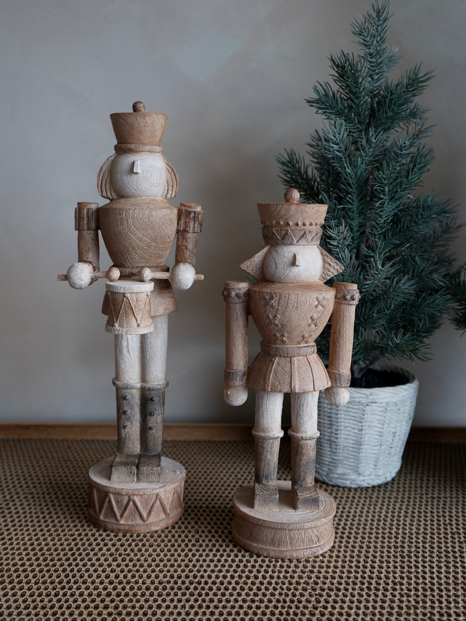 Two wooden nutcrackers on a textured surface with a potted plant in the background.