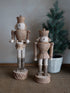 Two wooden nutcrackers on a textured surface with a potted plant in the background.