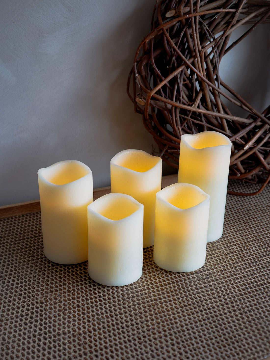 Set of five white candles on a textured surface with a wicker ball in the background.