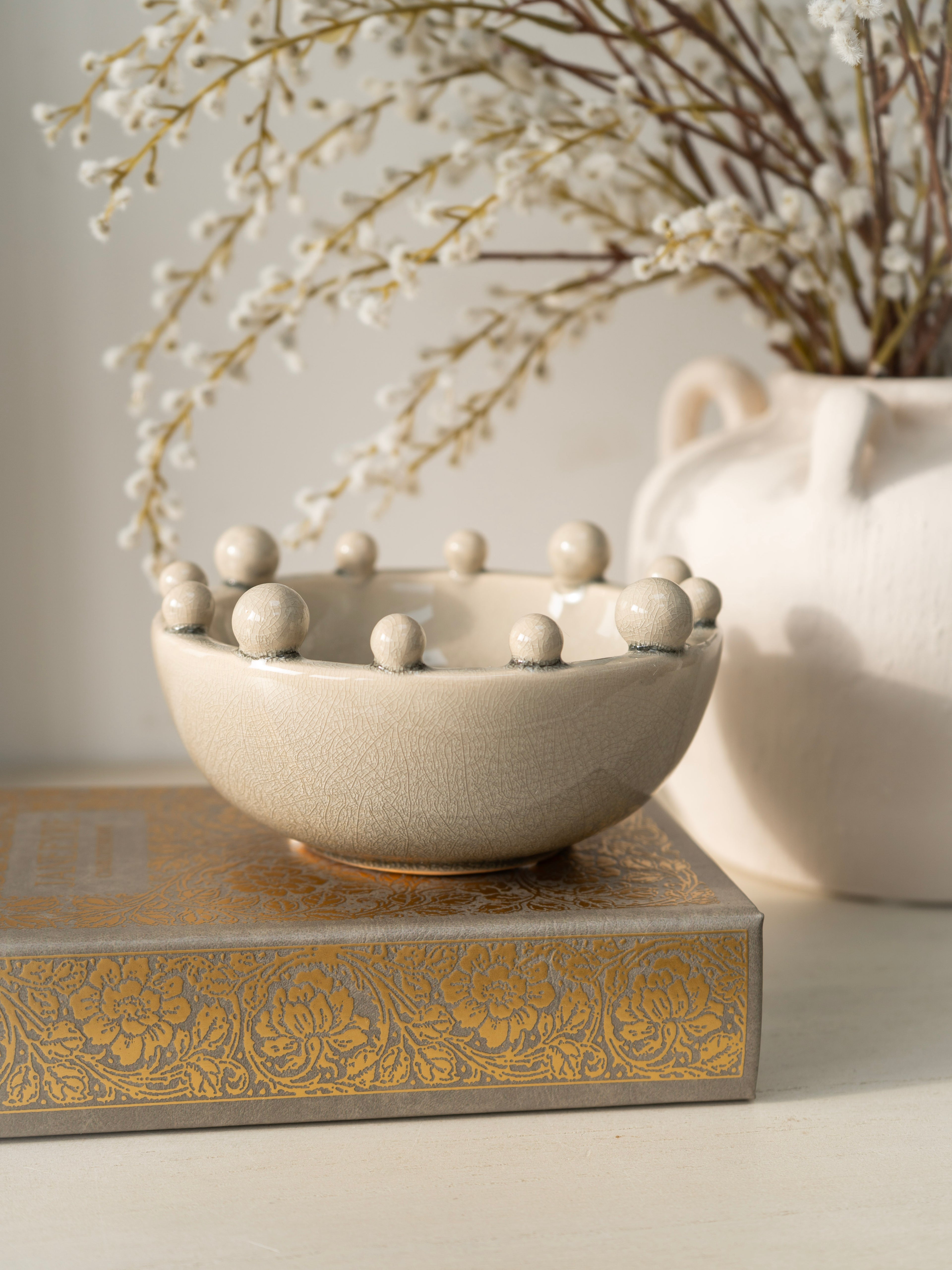 Decorative bowl with spherical elements on a textured surface with a vase in the background