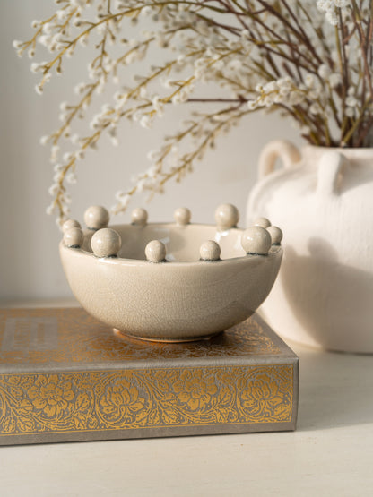 Decorative bowl with spherical elements on a textured surface with a vase in the background