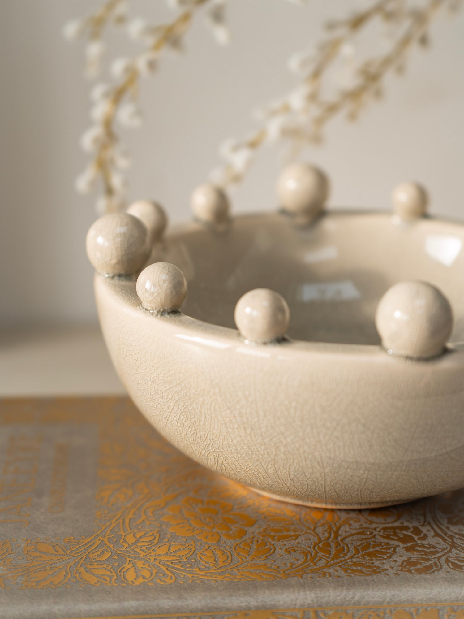Cream ceramic bowl with spherical bobble protrusions on a decorative surface