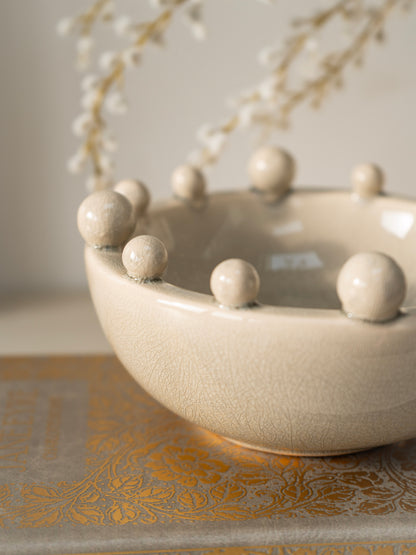 Cream ceramic bowl with spherical bobble protrusions on a decorative surface