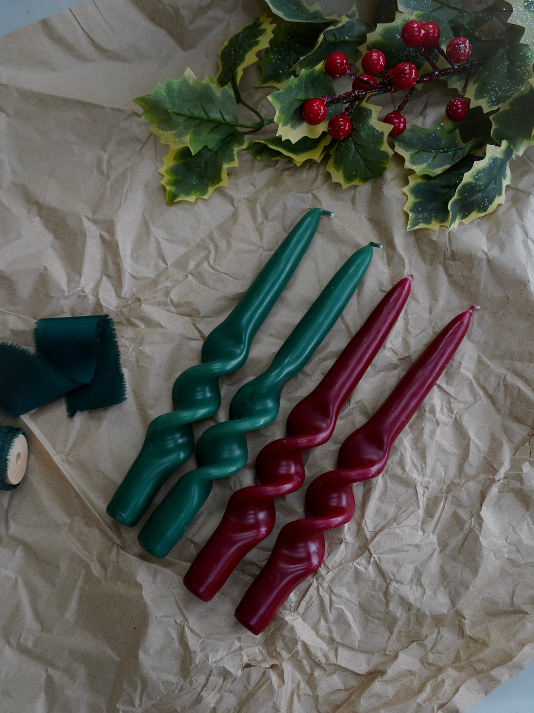 Set of green and red spiral candles on crumpled paper with holly leaves and berries.