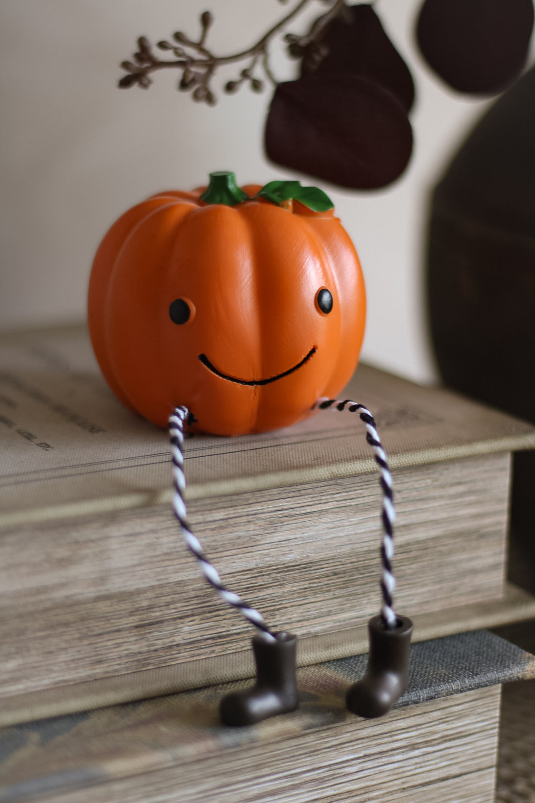Pumpkin with a face and legs on a stack of books, with Halloween decorations in the background.